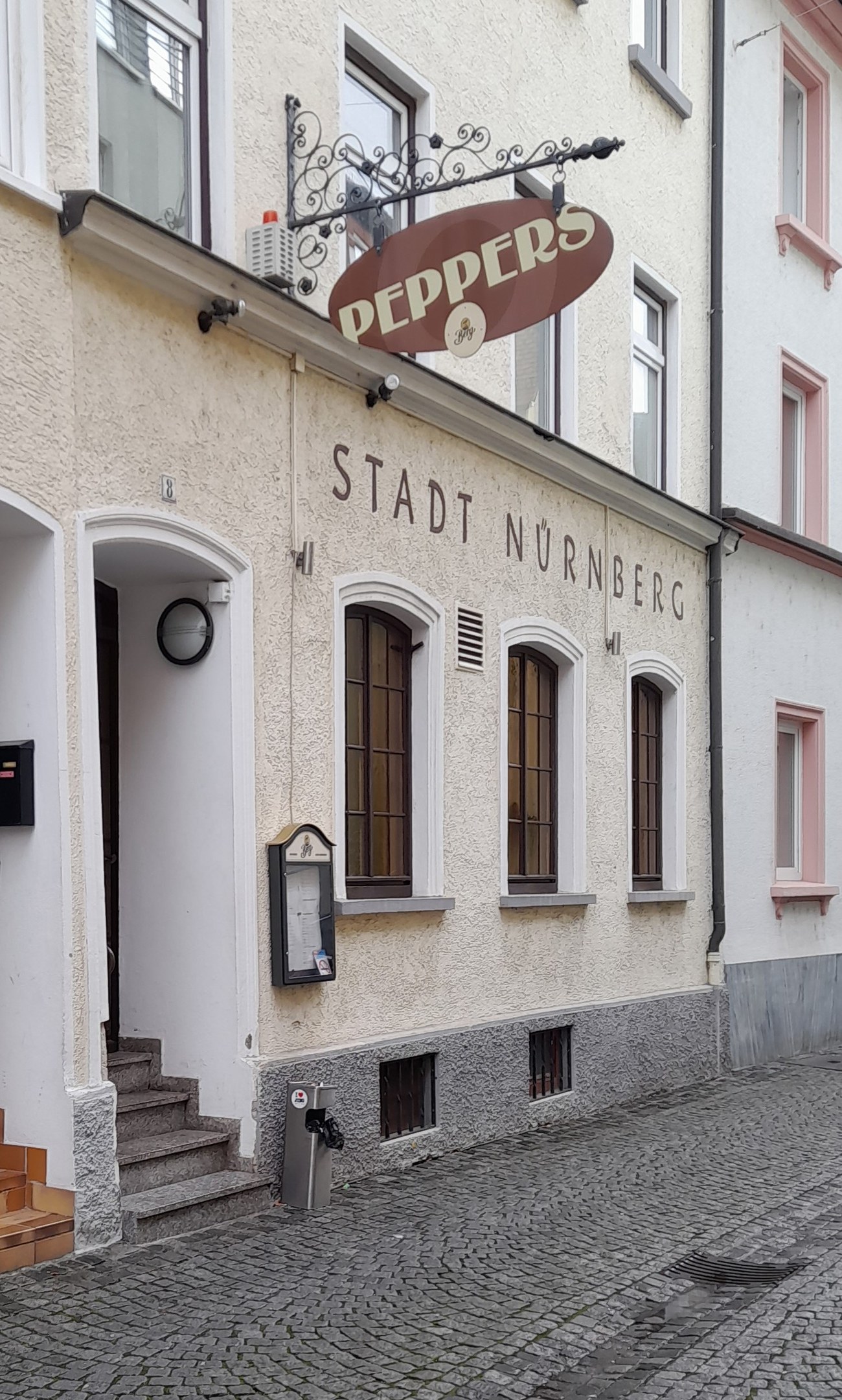 Außenseite eines Gebäudes mit einem "Stadt Nurnberg"-Schild, Fenstern, einer Tür, einer Treppe und einem Müllcontainer im Vordergrund.
