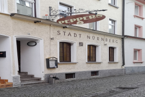 Außenseite eines Gebäudes mit einem "Stadt Nurnberg"-Schild, Fenstern, einer Tür, einer Treppe und einem Müllcontainer im Vordergrund.