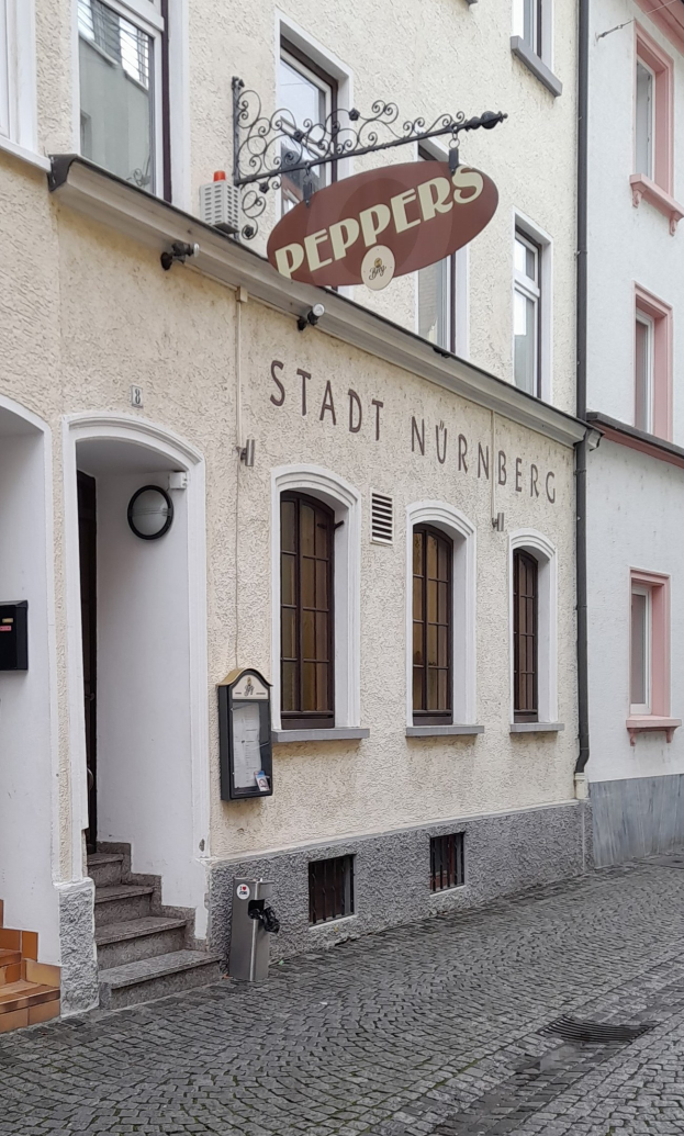 Außenseite eines Gebäudes mit einem "Stadt Nurnberg"-Schild, Fenstern, einer Tür, einer Treppe und einem Müllcontainer im Vordergrund.