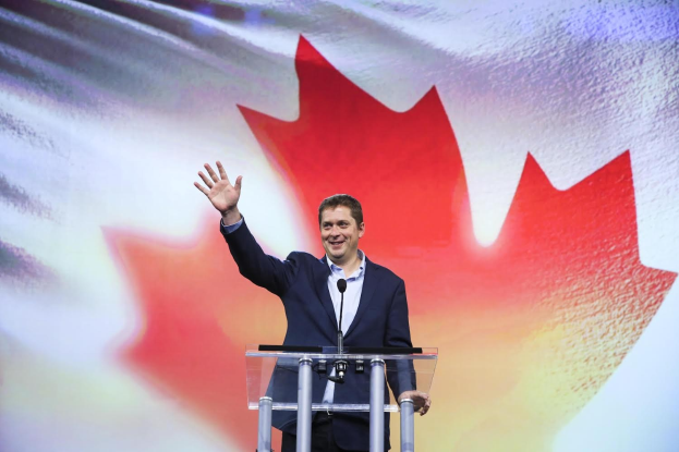 Der kanadische Premierminister Alex Salmond steht an einem Podium mit Mikrofonen, lächelt vor einer kanadischen Flagge, mit einem sichtbaren Bildschirm im Hintergrund.