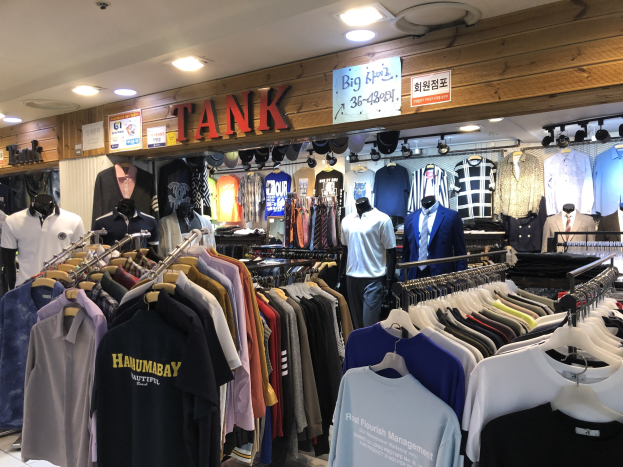 Ein modernes Bekleidungsgeschäft mit zahlreichen auf Ständern und Schaufensterpuppen präsentierten T-Shirts, mit beleuchteter Decke und informativen Texttafeln an den Wänden.