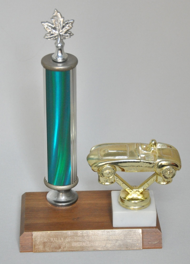 Ein Pokal mit einem glänzenden, detailreich verzierten Auto darauf, auf einer hellen Holzplatte montiert.