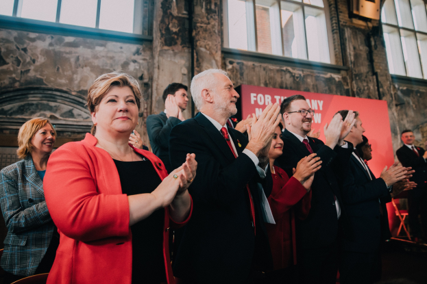 Eine Gruppe von Menschen, die vor einem Publikum jubeln, mit einem Banner "Wahlsieg" im Hintergrund.