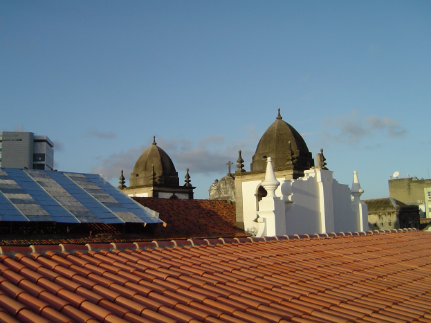 Stadtansicht mit ein paar Gebäuden im Vordergrund, einem blauen Himmel im Hintergrund und Solarpanelen auf einem Dach.