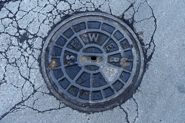 Ein Metall-Schachtobjekt am Straßenrand mit sichtbaren Rissen und eingravierter Schrift.