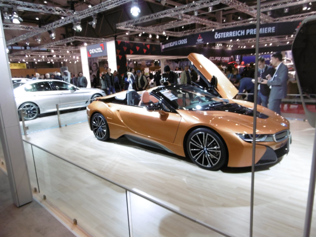 Ein elegantes schwarzes BMW i8 Roadster mit Chromakzenten und einem modernen Innenraum, das auf der Frankfurter Motor Show umgeben von formell gekleideten Gästen gezeigt wird.