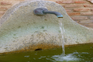 Ein steinerner Brunnen mit fließendem Wasser in einen Pool, vor einer Backsteinwand, schafft eine friedliche Atmosphäre.