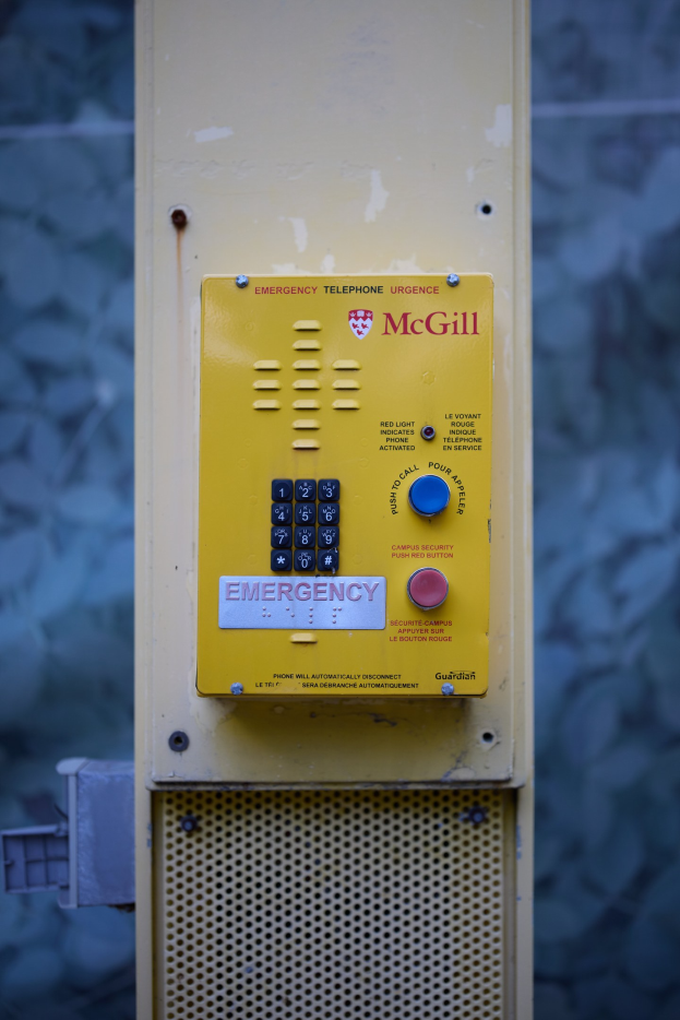 Ein gelbes Notfall-Telefon an einer Gebäudeseite angebracht, mit Tasten und Text für Notrufe, vor einer Wand.