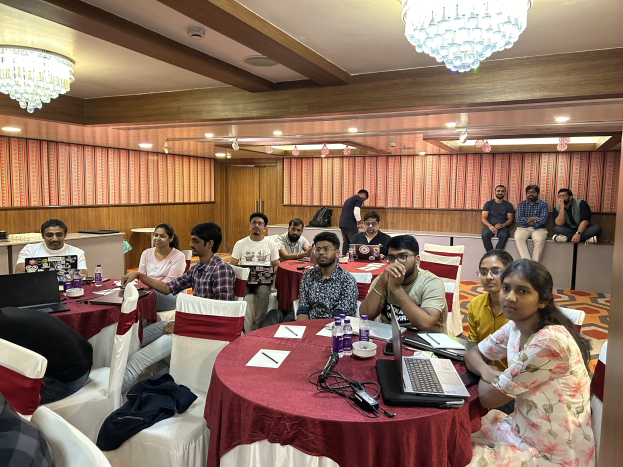 Gruppe von Menschen an einem Tisch mit Laptops und Utensilien während eines Online-Geld-verdienen-Workshops in einem beleuchteten Raum.