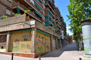 Eine Szene mit Gebäuden mit Fenstern, grüner Kleidung, Geschäften, Schildern und umgebenden Bäumen und Pflanzen.