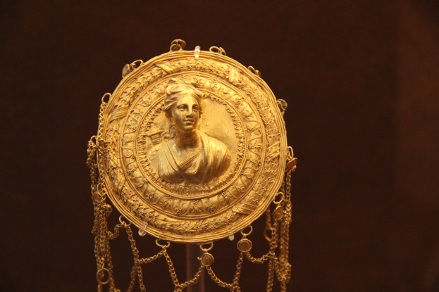 Goldene Medaille mit einer Frauengestalt, mit detaillierten Verzierungen auf dunklem Hintergrund.