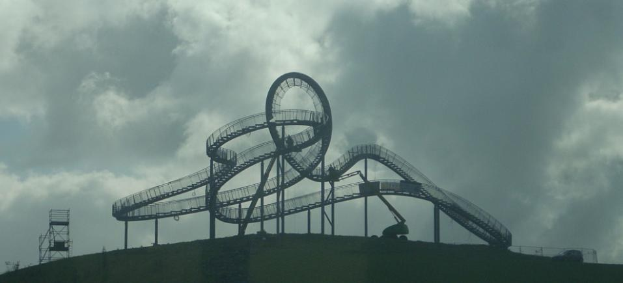 Eine Achterbahn auf dem Höhepunkt eines Hügels unter einem bewölkten Himmel, mit tragenden Pfählen und Strukturen.
