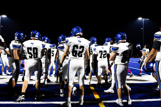 Eine Gruppe von Fussballspielern in Helmen und Stutzen steht auf einem Feld unter Flutlicht, bereit für ein Spiel.