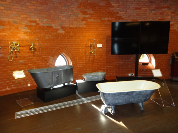 Ein gemütliches Badezimmer mit einer Ziegelwand, einer zentralen Wanne, an der Wand montierten Wasserhähnen auf der linken Seite und einem an der Wand montierten Fernseher auf der rechten Seite.