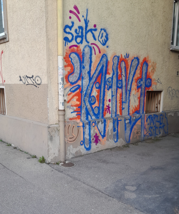 Ein Gebäude mit Fenstern, einem Rohr und Graffiti an der Seite, mit einer Straße am unteren Ende des Bildes.