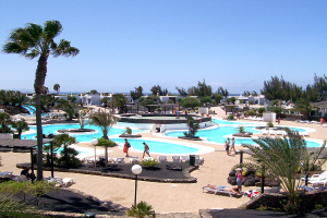 Ein Resort mit Pools umgeben von Bäumen, Menschen zwischen den Pools spazieren, Gebäude im Hintergrund und ein klarer Himmel darüber.