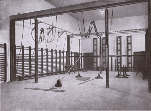 Schwarzes und weißes Foto eines Gymnastikraums mit verschiedenen Geräten auf dem Boden, Fenstern im Hintergrund und Text unten.