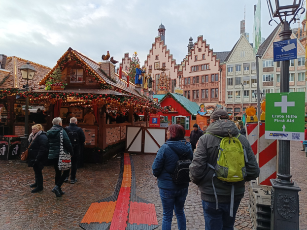 Menschen, die auf einem Kopfsteinpflasterweg neben einem Weihnachtsmarkt in Nürnberg, Deutschland, gehen, mit Laternenmasten, Texttafeln und Gebäuden im Hintergrund.