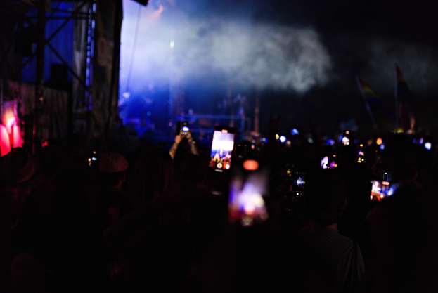 Eine Menge bei einem Konzert hält beleuchtete Handys hoch, während Bühnenlicht und Rauch eine lebendige Atmosphäre schaffen.