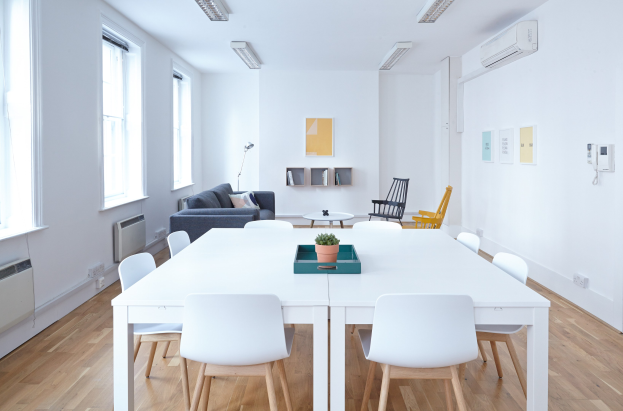 Wohnungsinneneinrichtung mit weißem Tisch und Stühlen, einer Pflanze in einer Schale, einem Sofa mit Kissen, einer Lampe, Regalen mit Gegenständen, einer Klimaanlage, Fotorahmen an der Wand, Fenstern und Deckenleuchten.