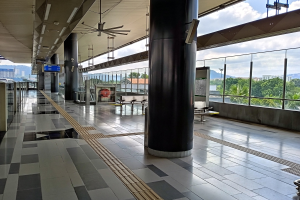 Leerer Flughafen-Terminal mit großen Fenstern, die auf eine Stadt blicken, mit Säulen, Schildern, Lampen, Ventilatoren und einer Aussicht auf Bäume, Gebäude, Hügel und bewölkten Himmel.