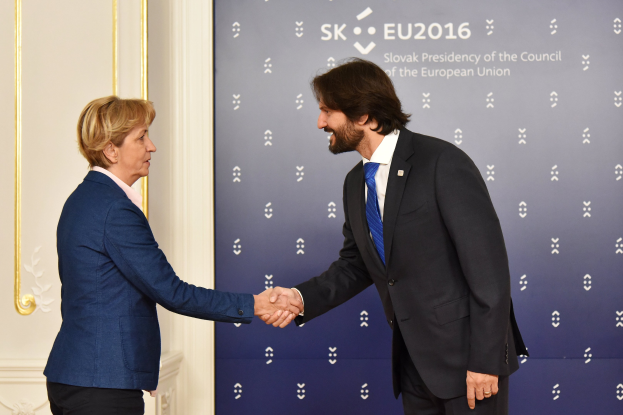 Bundeskanzlerin Angela Merkel und Bundeskanzler Joachim Gauck schütteln sich die Hände bei einem EU-Gipfeltreffen, lächeln und stehen vor einem Banner mit der Aufschrift "EU-Gipfel" und einer Tür im Hintergrund.