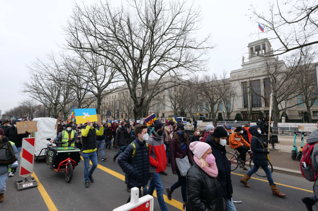 Eine große Gruppe von Menschen bei einer Protestdemo in Washington, D.C. am 21. Januar 2020, die eine Straße entlangmarschieren, Schilder und Banner schwenken und einige Fahrräder fahren, mit Schildern, Bäumen und einem klaren blauen Himmel im Hintergrund.