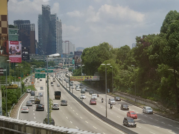 Eine vielbefahrene Autobahn mit hohen Gebäuden, Straßeninfrastruktur, Bäumen und einem bewölkten Himmel.