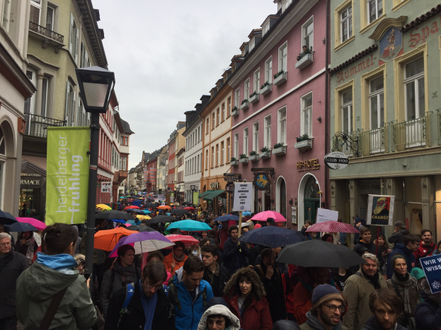 Große Gruppe von Menschen, die eine Straße mit Schirmen und Schildern entlanggehen