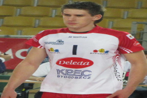 Ein Mann in einem rot-weißen Handballtrikot steht auf einem Feld, umgeben von Zuschauern, mit einem roten Banner im Hintergrund, auf dem "Krasnoyarsk vs Bydgoszcz" steht.