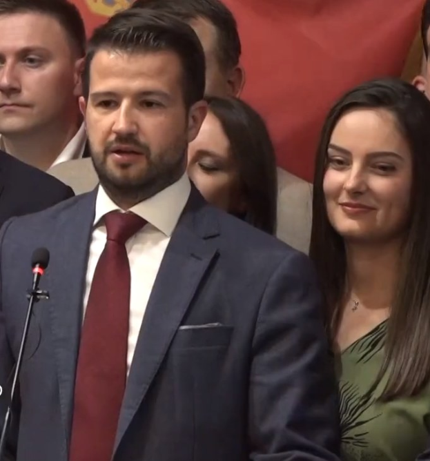 Ein Mann in Anzug und Krawatte spricht in ein Mikrofon an einem Podium, mit einem Banner dahinter und einer Menge davor, wahrscheinlich zu einem sozialen Medienverbot.