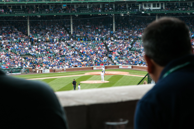 Baseballspiel in einem Stadion mit Menschen auf dem Feld im Vordergrund und Zuschauern in den Rängen.