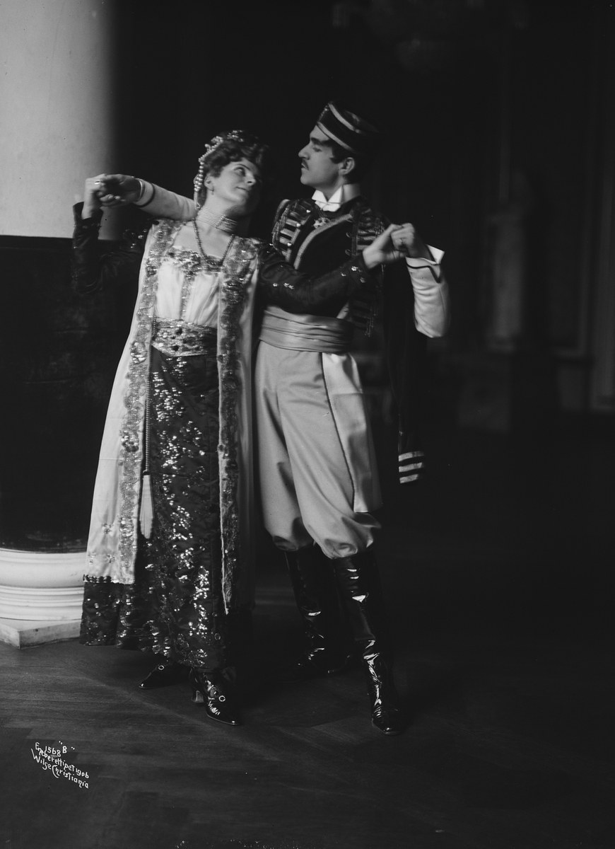 Schwarzes und weißes Foto eines Mannes und einer Frau, die in einem Ballsaal tanzen, mit einer Säule und einer Wand im Hintergrund, der Mann trägt Schuhe, die auf eine Vorstellung hinweisen.