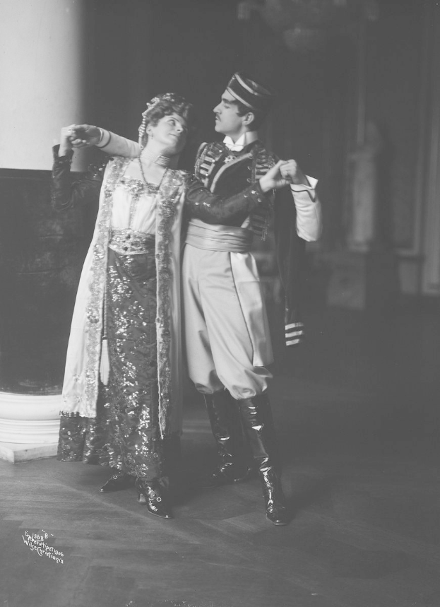 Schwarzes und weißes Foto eines Mannes und einer Frau, die in einem Ballsaal tanzen, mit einer Säule und einer Wand im Hintergrund, der Mann trägt Schuhe, die auf eine Vorstellung hinweisen.