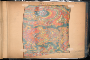 Ein aufgeschlagenes Buch mit einem bunten Teppich darauf, das ein Stück Papier mit darauf geschriebenem Text enthält.