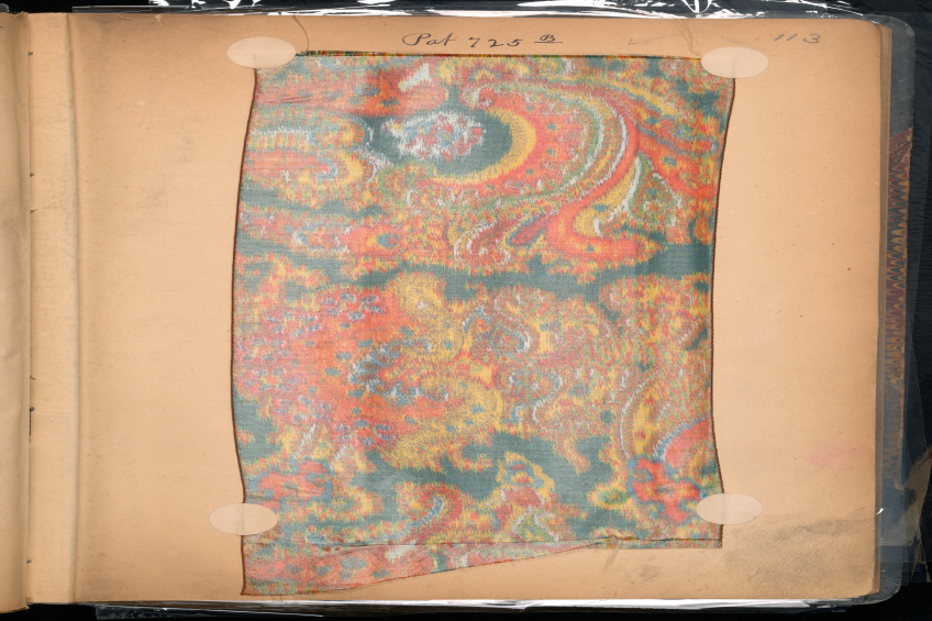 Ein aufgeschlagenes Buch mit einem bunten Teppich darauf, das ein Stück Papier mit darauf geschriebenem Text enthält.