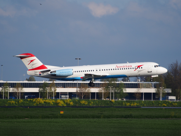 Austrian Airlines Airbus A320-200 beim Start vom Frankfurt Airport mit Grünfläche, Gebäude und bewölktem Himmel im Hintergrund.
