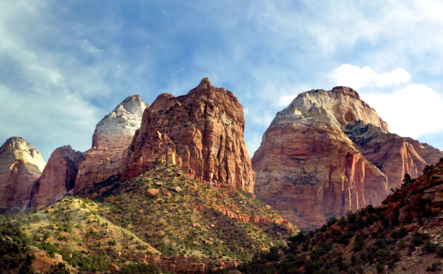 Zion National Park in Utah mit majestätischen Bergen, üppigen Bäumen, steinigem Gelände und weißen Wolken am Himmel.