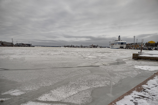 Großes Kreuzfahrtschiff liegt im verschneiten Hafen mit Gebäuden, Bäumen und bewölktem Himmel im Hintergrund.