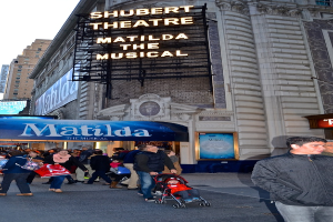 Eine Gruppe von Menschen steht in der Nähe von Gebäuden und Plakaten, mit einem Baby im Kinderwagen.