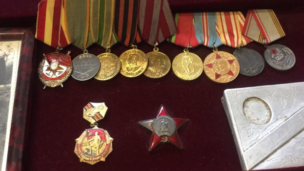 Eine hölzerne Box mit verschiedenen Medaillen, darunter ein roter Sternsymbol, ordentlich mit einem Objekt auf der rechten Seite.