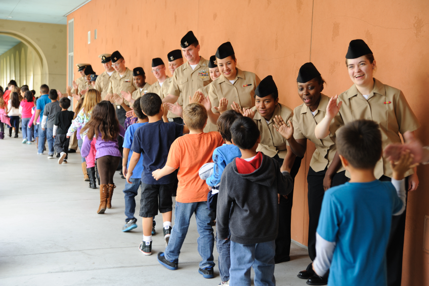 Eine Gruppe von Kindern in Uniformen, die einen Flur entlanggehen, mit einer Wand auf der rechten Seite und einer Decke mit Lampen oben.