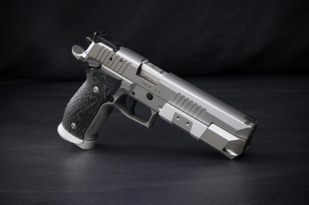 Eine Sig Sauer P226 X-Five 9mm Pistole auf einer schwarzen Oberfläche vor einem schwarzen Hintergrund.