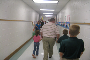 Menschen gehen in einem Gebäude mit Lampen oben und Papieren an der Wand im Hintergrund.