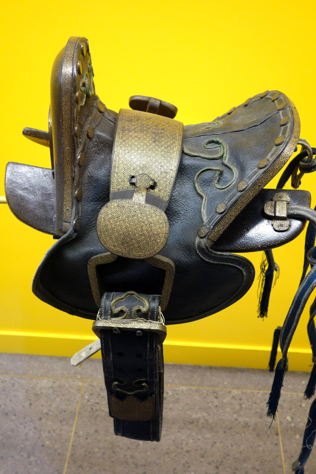 Nahaufnahme eines Pferdesattels, der in einem Geschäft mit einer gelben Wand im Hintergrund und dem Boden darunter ausgestellt ist.