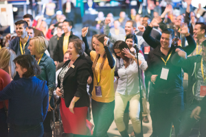 Eine Gruppe von Menschen, die mit einem Mikrofon auf einem Ständer in der Mitte stehen und lachen.