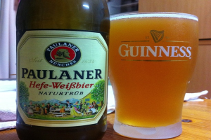 Eine Flasche mit einem beschrifteten Design von Bäumen, Menschen, Hügeln und einem Haus, ein Glas mit einer Aufschrift darauf und ein Handtuch liegen auf einem Tisch.