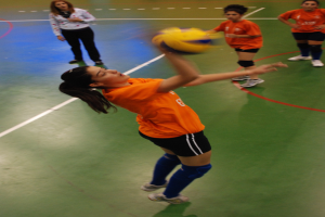 Eine Volleyballspielerin schlägt den Ball, während zwei andere Spieler und eine weitere Frau zusehen.