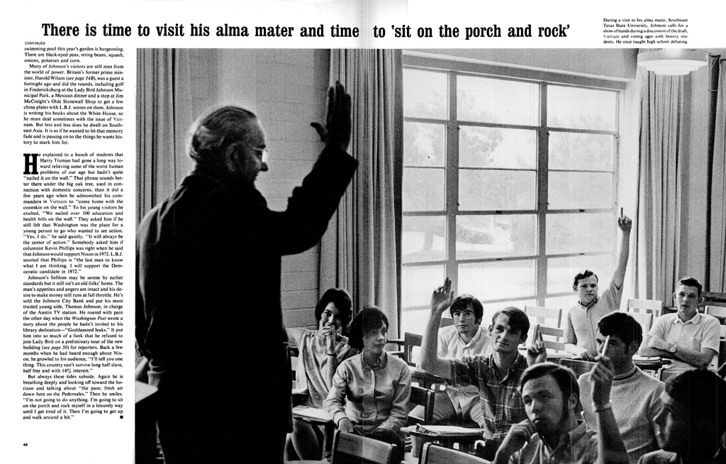 Eine Person mit Brille steht vor einer Gruppe sitzender Personen, mit einer Vorhangwand und Fenstern im Hintergrund.