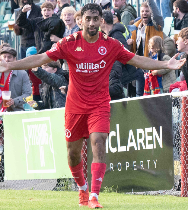 Ein Fussballer in roter Uniform rennt mit ausgestreckten Armen auf einem Feld, mit einer Menge im Hintergrund und einem Banner mit der Aufschrift "Middlesbrough FC v Swansea City - Sky Bet Championship" im Vordergrund.